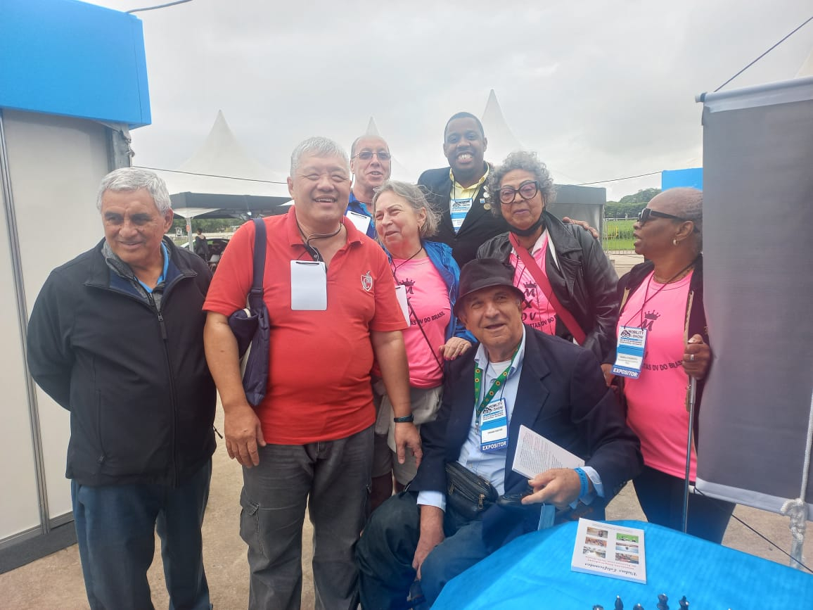 Nós mulheres enxadristas de camisetas rosas, e os meninos que nos auxiliaram na feira. Tendo Osmar Santos no centro com chapéu escuro. Todos estamos sorrindo